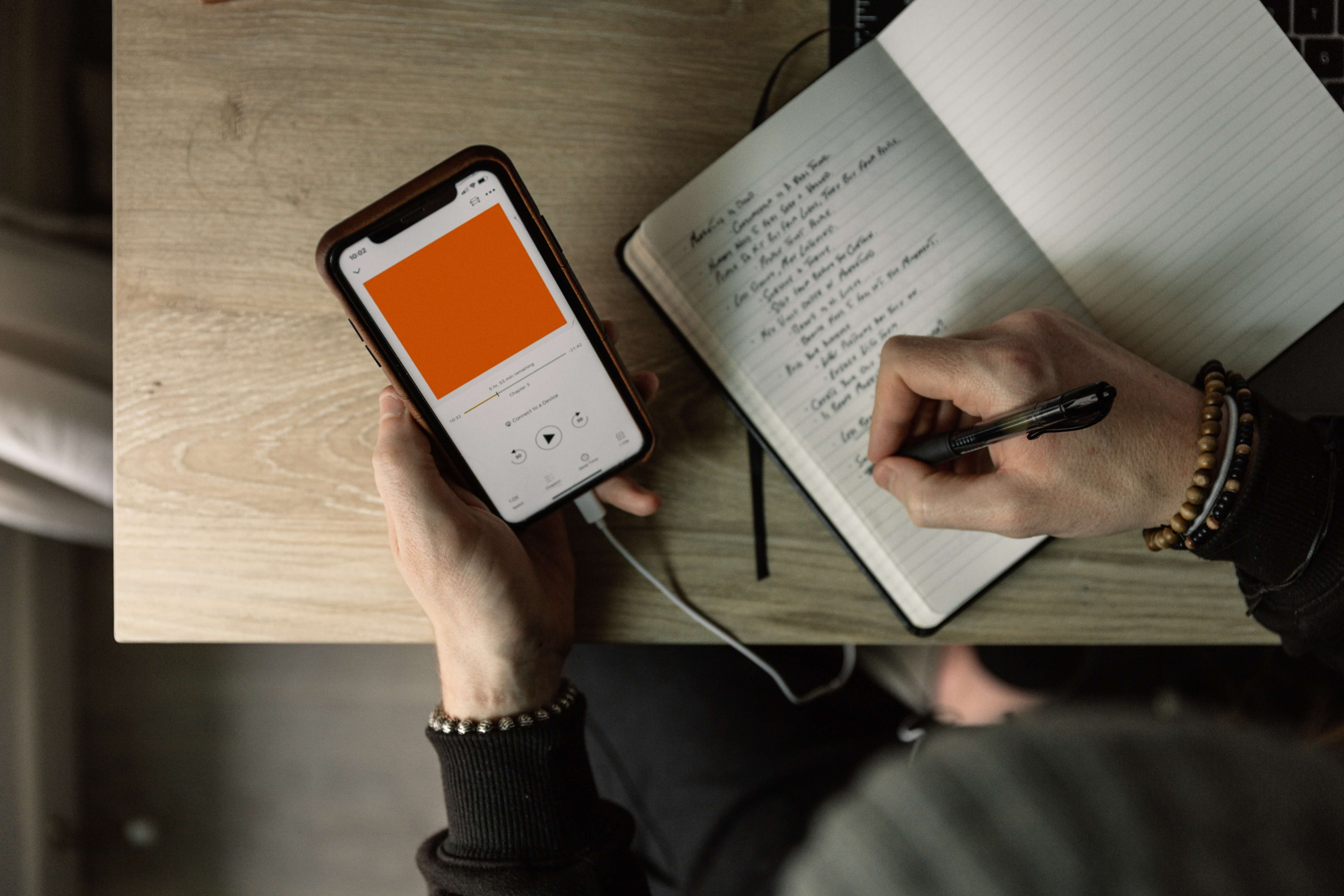 person writing on notebook and holding phone